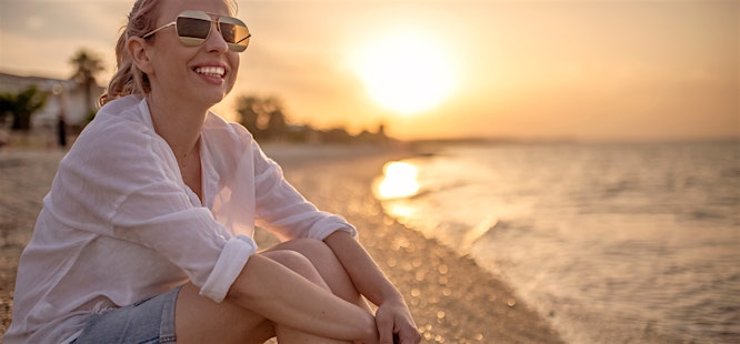 woman wearing sunglasses at the beach and sunscreen following dermatologist advice