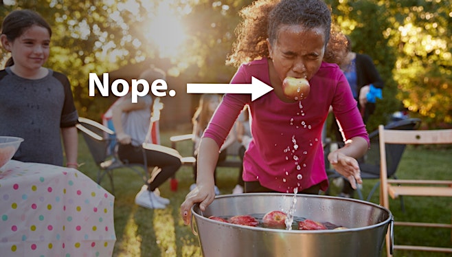 girl in pink shirt bobbing for apples outside at party