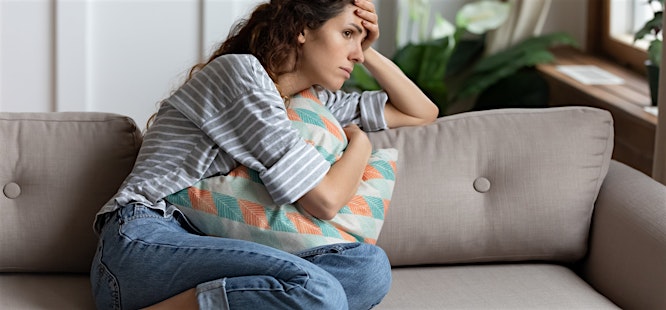 woman sitting on the couch feeling stressed and sick and needs to see primary care doctor
