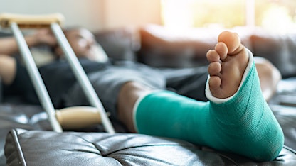 man reclining on couch with green cast on broken foot after going to urgent care