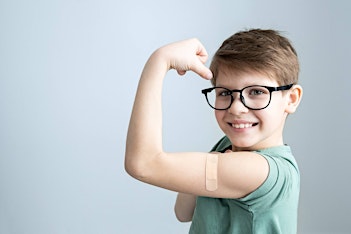 Child wearing glasses showing arm after vaccine