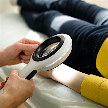 dermatologist using a magnifying glass for skin cancer screening on female patient