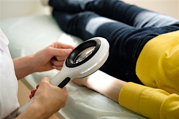 dermatologist using a magnifying glass for skin cancer screening on female patient